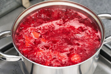 Boiling red borscht soup with beetroot and vegetables in metal pot. Traditional homemade dish for dinner. Polish cuisine with natural ingredients and rich color.