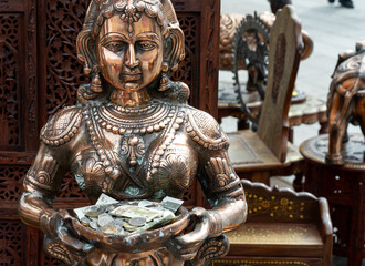 Bronze statue of Indian goddess holding coins and banknotes as offerings, traditional Hindu art sculpture with detailed craftsmanship