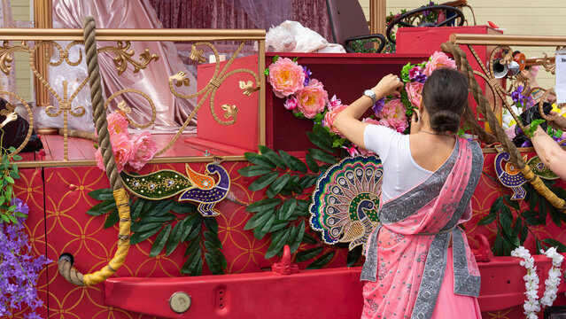 Woman in traditional pink sari decorating colorful festival parade float with flowers and peacock ornaments during cultural celebration