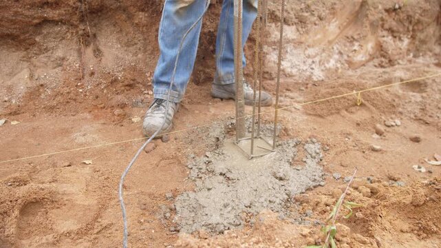 technician uses cable vibrator for concrete smoothing, technician carefully smooths and levels newly poured concrete at column base using cable vibrators and tools for structural integrity
