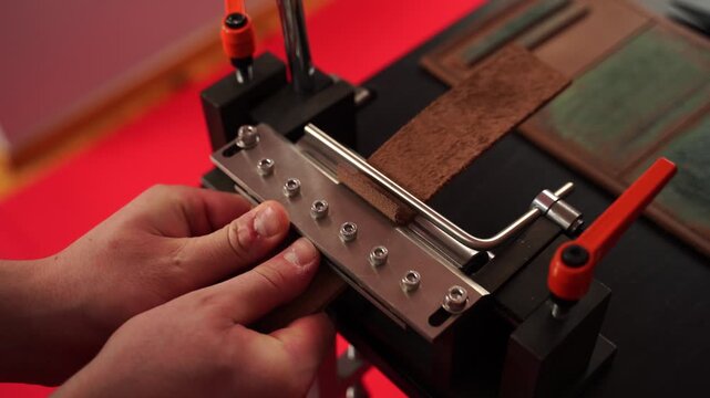 4k Video Leatherworker uses a creasing press to refine strap edges, adding detail and smoothness for handcrafted products. Craftsman shapes a leather strap with an edge creasing machine.
