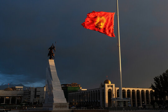 Bishkek, Kyrgyzstan - August 04, 2025: The flag of Kyrgyzstan on a 100-meter flagpole, lowered due to the evening hurricane wind, on the main square of the capital Ala-Too with a new monument to Manas