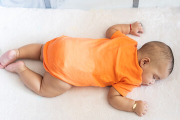 Baby sleeping peacefully on white blanket wearing orange onesie