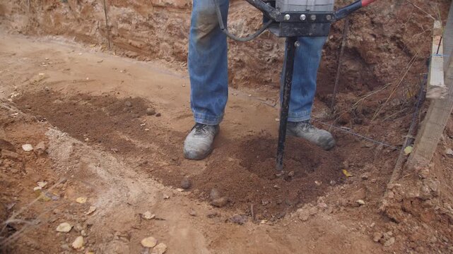 foundation crew drilling deep footing with heavy auger, twohanded operation and steady stance, large soil clods ejected into pile, professional construction rhythm and measured spacing