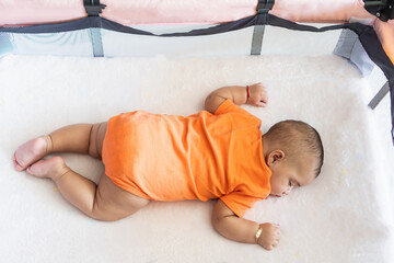 Baby sleeping peacefully on tummy in playpen crib