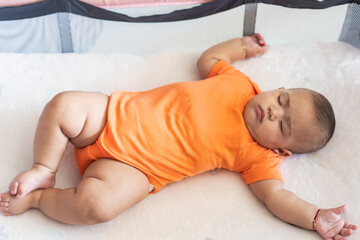Baby infant sleeping peacefully in crib wearing orange