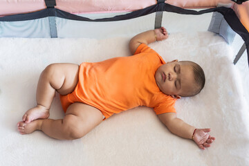 Baby peacefully sleeping in crib wearing orange onesie
