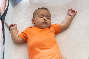Baby sleeping peacefully in crib wearing orange onesie