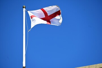 Flag of England - red cross on the white backdrop - against the clear blue sky. Patriotic symbols concept.