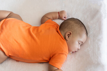 Baby sleeping peacefully in orange onesie on white surface