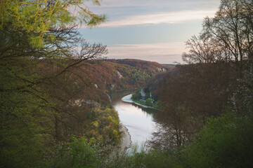 Danube gorge Kelheim in soft evening light, serene river bend between limestone cliffs and spring forest, framed by branches, ideal for travel ads.