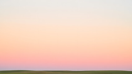 Serene sunset landscape with pastel gradient sky over green field in soft focus