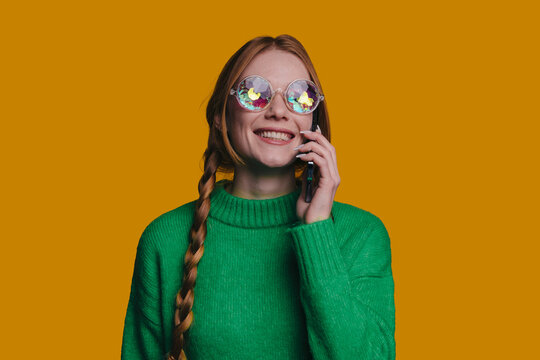 A Happy Woman Wearing a Green Sweater and Colorful Glasses While Engaged on Her Phone