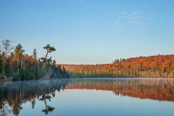Beautiful calm northern Minnesota lake below hills in fall color on a clear autumn morning