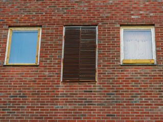 Brick wall with uneven windows and central metal shutter.