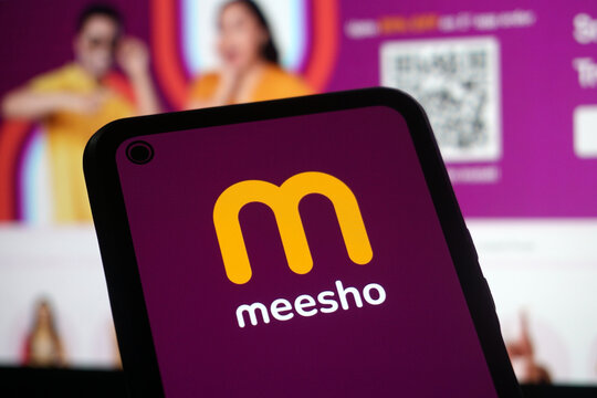 Meesho App Logo on Smartphone with Website in Background