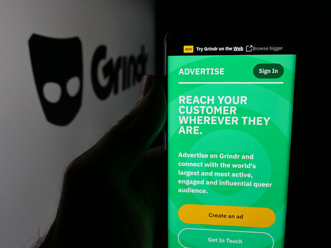 Stuttgart, Germany - 10-15-2025: Person holding cellphone with webpage of LGBT social media platform company Grindr Inc on screen in front of logo. Focus on center of phone display.