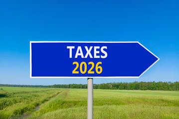 Taxes 2026 new year symbol. Concept words Taxes 2026 on beautiful blue road sign. Beautiful green grass field forest and blue sky background. Business and taxes 2026 new year concept. Copy space.