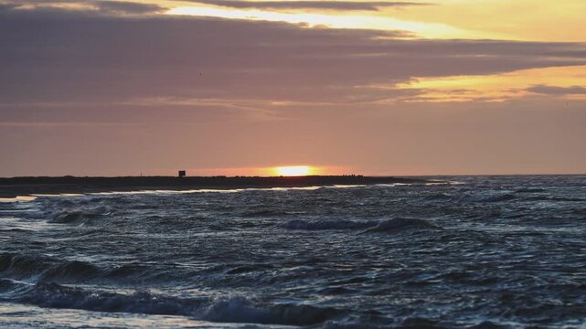 Golden sunset light bathes the northern Danish coast, where shorebreak waves meet a wide sandy beach