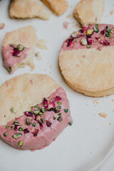 Two cookies with pink frosting and rose petals on top