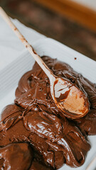 A wooden spoon is used to scoop up a thick, gooey chocolate mixture