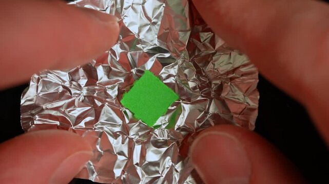 Hands of the person at the party or dance club open or tear foil with LSD strip blotter with dry drop of Lysergic acid drug lucy. Hallucinogenic drug in the foil for consumption.