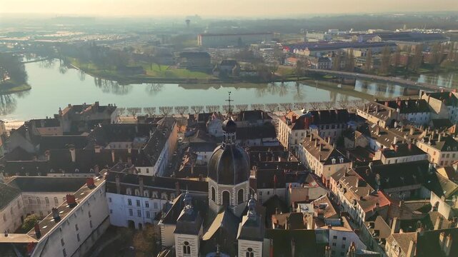 Drone footage showing baroque church and traditional tiled roofs with waterway and urban area under soft morning glow 