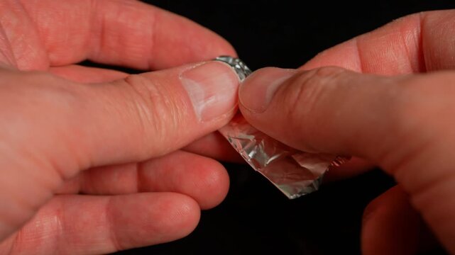 Hands of the person at the party or dance club open or tear foil with LSD strip blotter with dry drop of Lysergic acid drug lucy. Hallucinogenic drug in the foil for consumption.