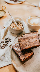 A plate of brownies sits on a table next to a cup of coffee