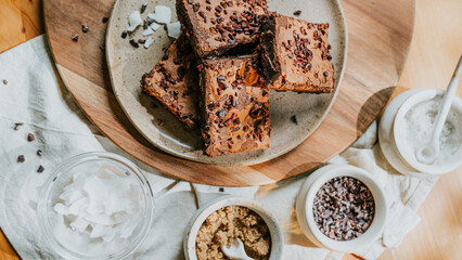 A plate of brownies sits on a wooden table with a white cloth underneath
