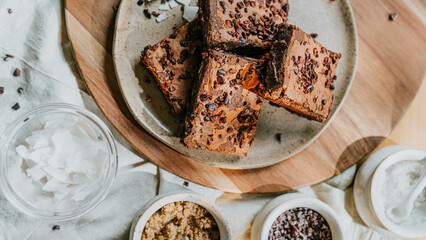 A plate of brownies sits on a wooden table with a bowl of coconut flakes