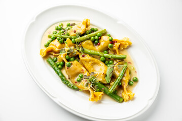 A plate of stuffed pasta with peas and asparagus in a creamy sauce, garnished with herbs and red peppercorns.