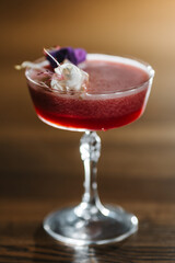 Elegant red cocktail in a crystal glass decorated with edible flowers on a wooden table. Fresh summer drink, luxury bar concept, mixology and lifestyle photography