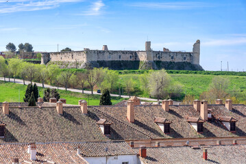 The weathered stone walls of the Castillo de los Condes (Castle of the Counts) stand atop a green...