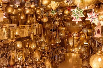 A wide variety of ornate, golden lamps and lanterns fill a shop in Morocco. The light fixtures are of different shapes, sizes, and styles, creating a warm ambiance.