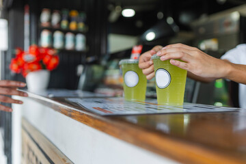 Hands serving green smoothies at a café counter, illustrating a takeaway beverage concept in a local business setting.