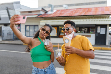 Latino friends taking a selfie and enjoying street food on a sunny day