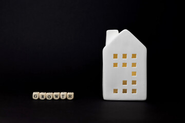 White ceramic house figurine beside wooden blocks spelling growth, symbolizing financial...