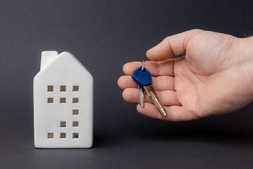 Hand holding keys near a ceramic house model, symbolizing investment in property and the importance of security and stability in real estate. copy space