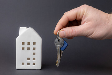 Hand holding keys above a ceramic house model, symbolizing home ownership and real estate investment in a modern financial context. copy space