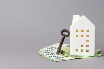 White ceramic house model with a vintage key resting on a stack of euro banknotes, symbolizing finance and real estate investment opportunities. copy space