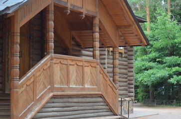 Fototapeta premium The porch of an Orthodox church. A wooden church stands among the pine trees on the site. The frame, doors, windows, walls, steps, and all the details are made of wood. The yellow wood has darkened.
