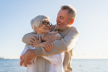 Senior mature couple hugging enjoying outdoor recreation walking on beach. Old husband wife...
