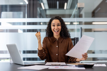 Young mixed race businesswoman celebrating achievement and feeling excited, holding success...