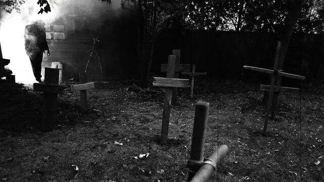 A zombie walking through a rustic cemetery graveyard with crosses and smoke Classic suspense horror or Halloween film theme. Edited with vintage silent film effects.