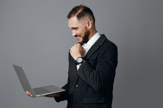 A professional businessman holds a laptop against an isolated colored background, demonstrating confident mood, focus, and subtle pride during a moment of achievement.