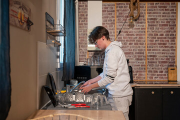 jeune homme faisant la vaisselle dans la cuisine de son appartement dans l'évier