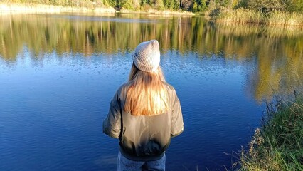 A young girl in a hat and a jacket looks at the lake.