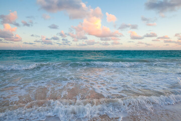 Bright beach scene features turquoise sea, gentle waves washing onto sandy shore