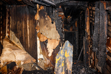 Charred interior of a fire-damaged room, displaying burnt wood, peeling wallpaper, and debris. A scene of destruction and aftermath